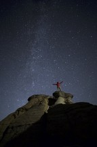 a man with open arms standing on a mountaintop under the stars in a night sky 
