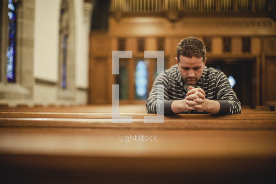 Man sitting in empty church pew praying