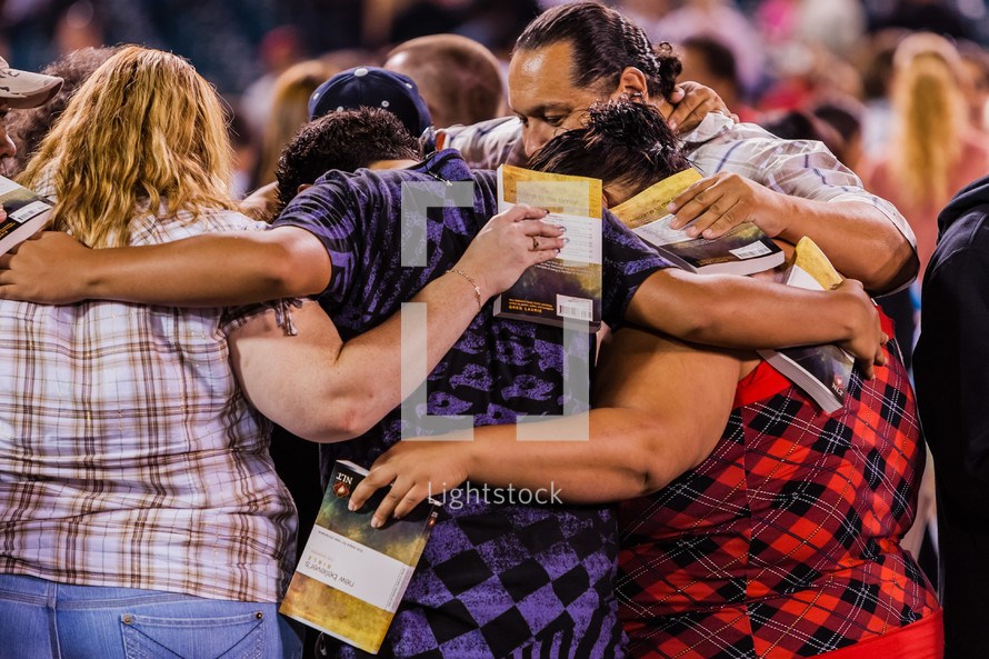 A group of people praying in a circle with arms around each other new believer salvation crusade