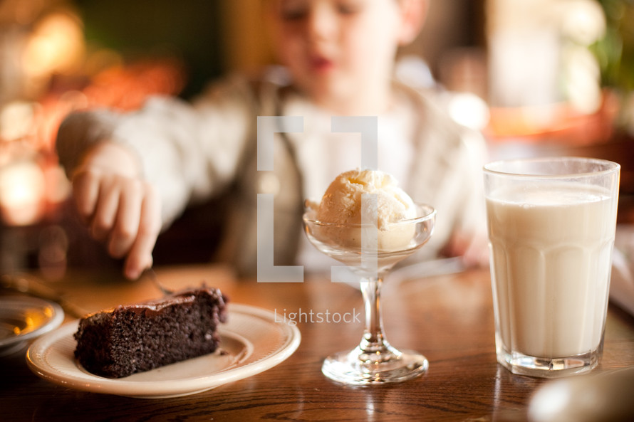 A boy in a restaurant enjoying chocolate cake, milk and ice cream.