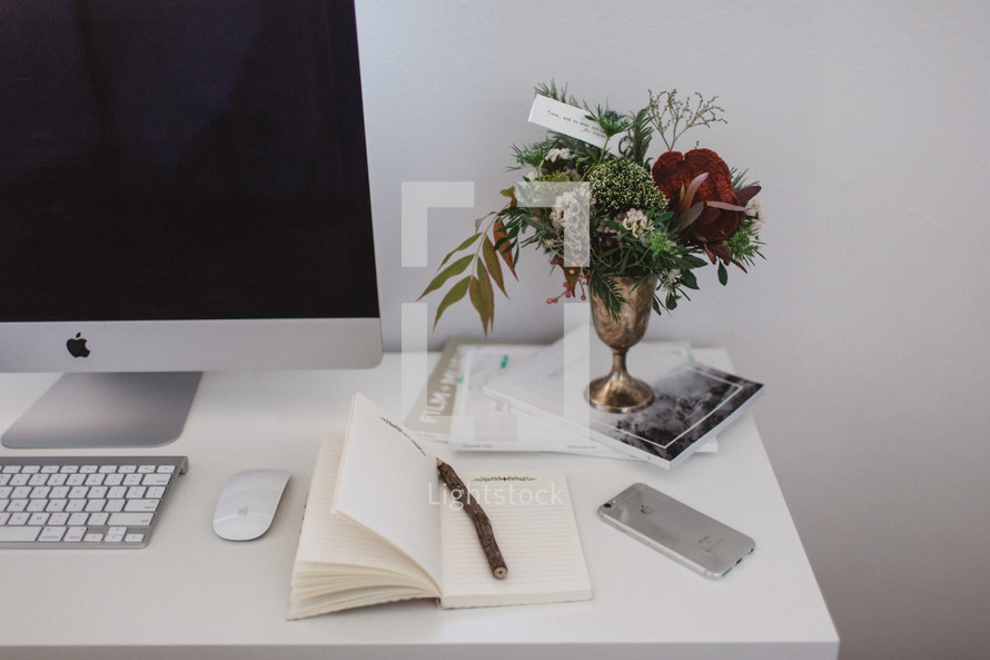 desk with notebook, computer, pencil, cellphone, books, and vase of flowers 