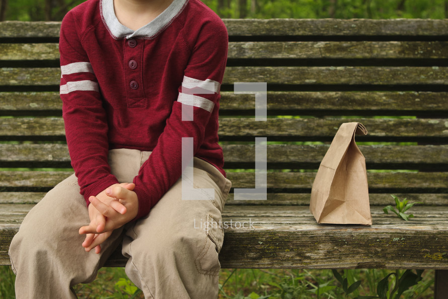 child sitting on a bench next to a brown bag 