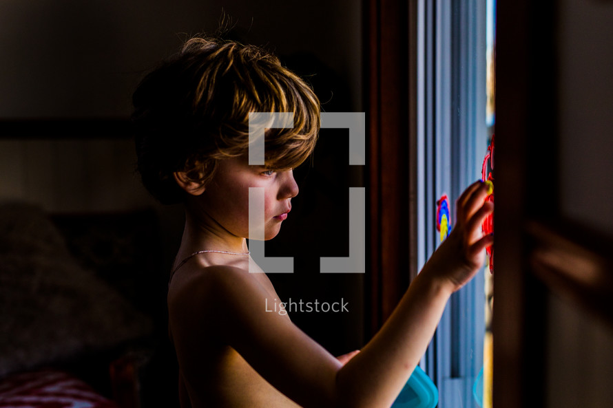 child finger painting on a window 