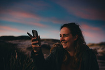 woman holding a cellphone taking a picture at sunset 