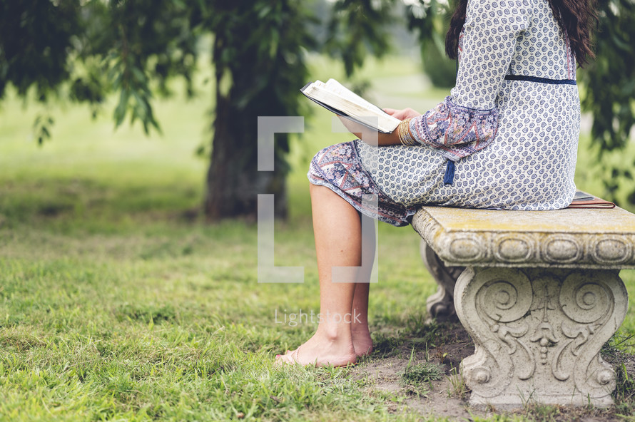 a woman sitting outdoors reading a Bible 