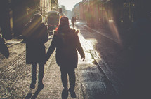 Rays of sun shining on two people walking down a cobbled street.
