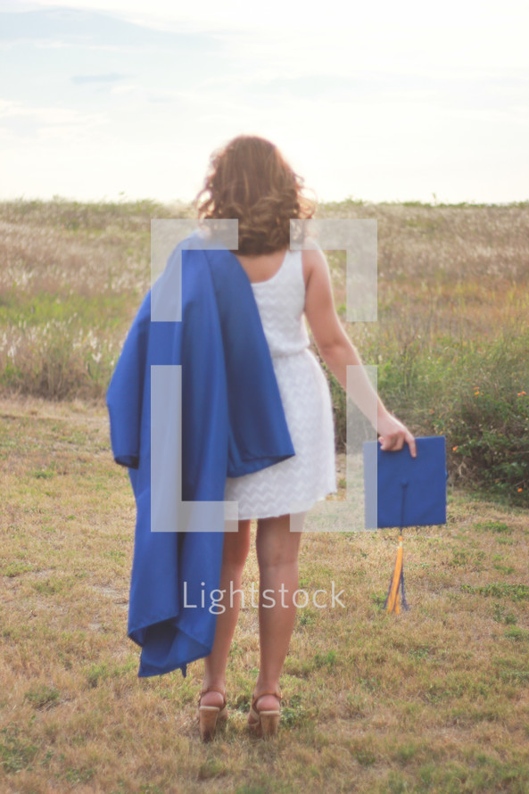 graduate in a dress holding her cap and gown outdoors 