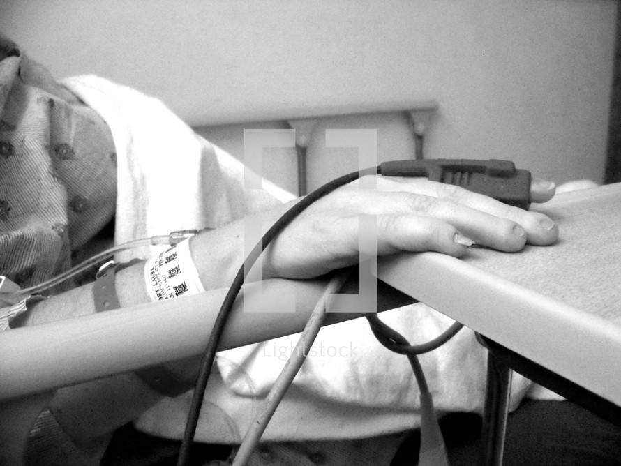 An up-close view of a hospital patient's hand sitting in a hospital bed after surgery. Black and white up-close photo. 