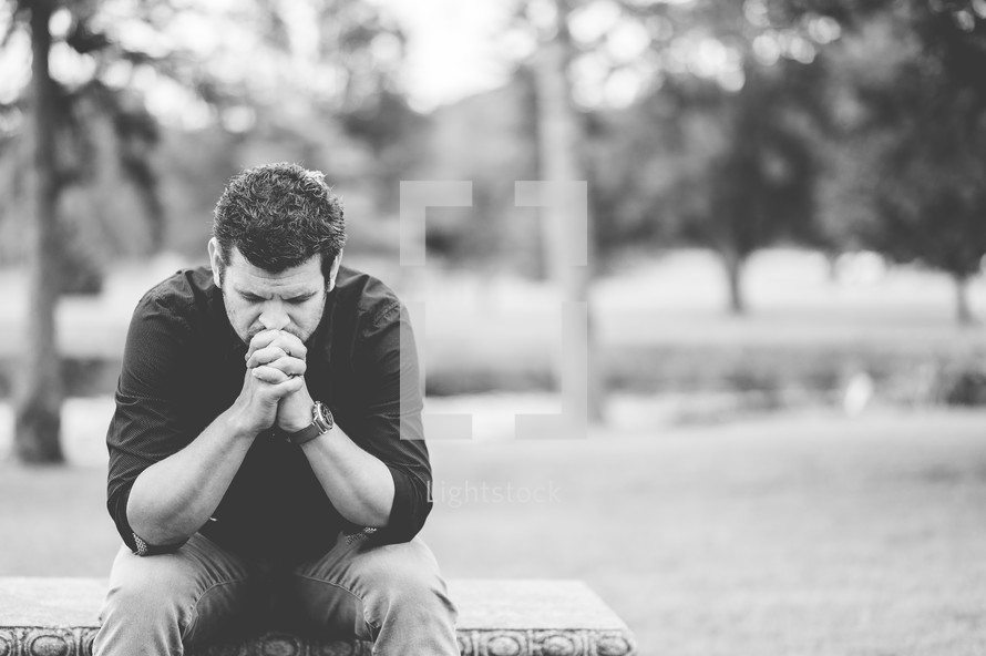 a man praying sitting outdoors 
