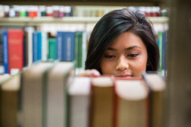 girl looking at books on a bookshelf in a library.