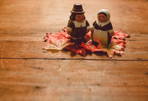 Pilgrim figurines on fall leaves on a wooden table -- Thanksgiving decor.
