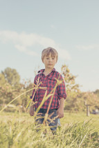 a boy child in a flannel shirt playing outdoors in tall grass 