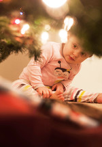 A toddler girl looking under a Christmas tree. 