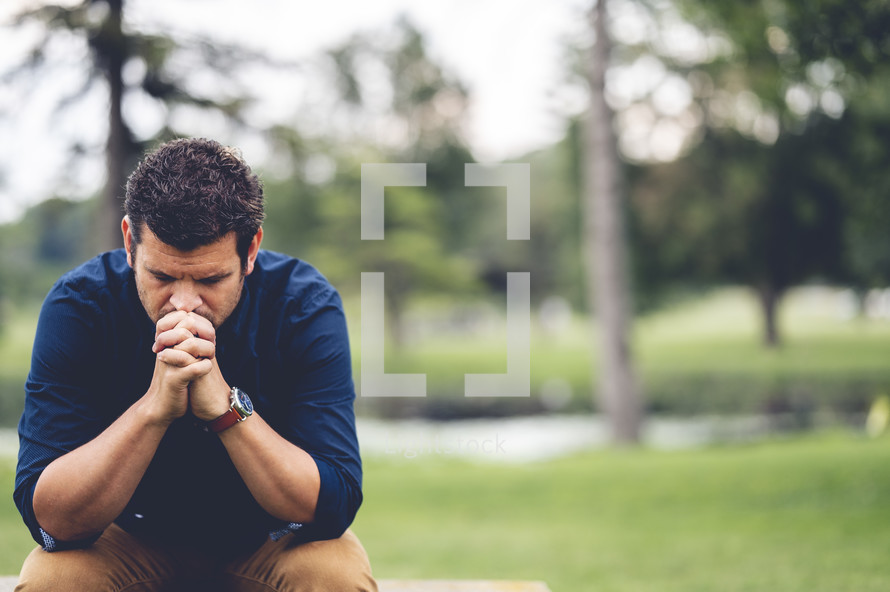 a man sitting outdoors praying 