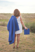graduate in a dress holding her cap and gown outdoors 