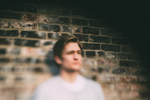 blurry image of a man leaning against a brick wall 