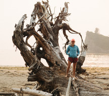 woman standing on driftwood on a beach 