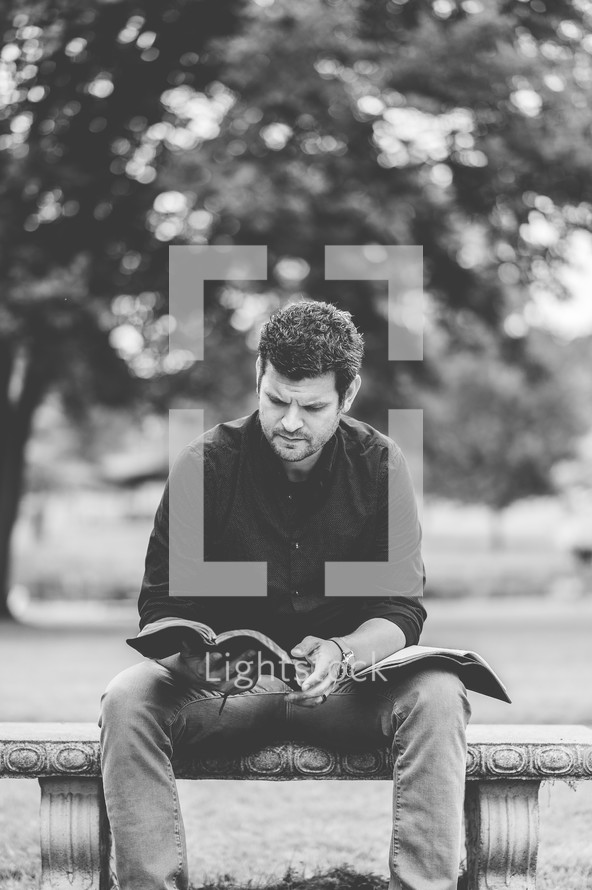 a man sitting outdoors reading a Bible 