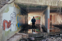 a man standing under concrete tunnels covered in graffiti 