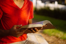 torso of a man reading a Bible outdoors 