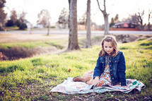 girl child sitting on a blanket in the grass