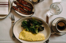 omelet, salad, greens, and bacon on a table 