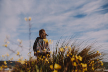 a girl standing on a beach and yellow flowers in the foreground 