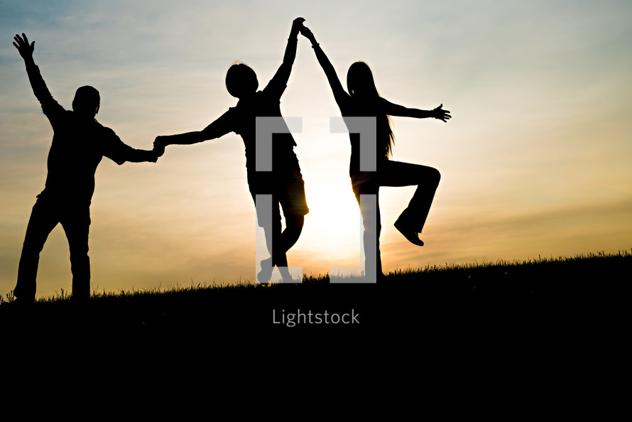 silhouettes of a father and his teenage children holding hands 