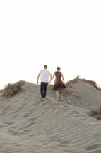 a couple walking up sand dunes holding hands