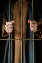 A man in Biblical garb holds onto prison cell bars.