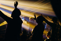 raised hands in an audience under the glow of spotlights 