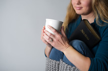 a woman sitting holding a mug of coffee and a Bible 