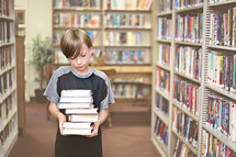 Boy carrying a stack of books in a library.