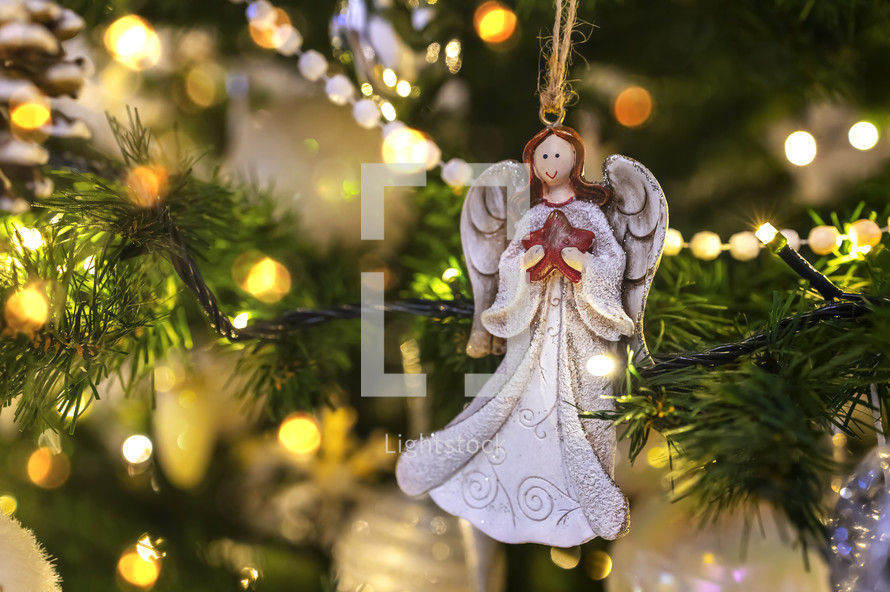 Angel ornament holding a star in a Christmas tree with lights