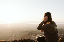 Woman drinking a beer while sitting and looking at a mountain sunset