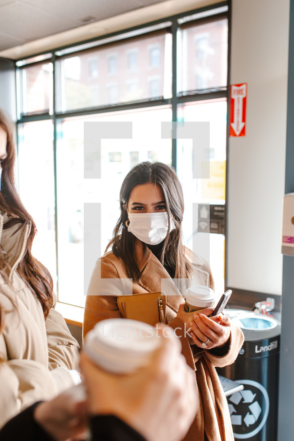 young women wearing face masks with coffee cups 