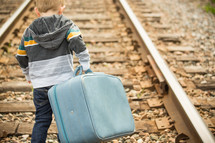 toddler carrying a suitcase on train tracks 