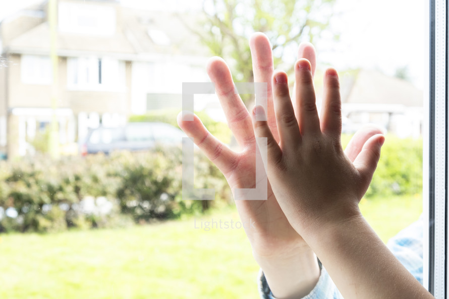 Boy holding his hand against glass mirroring his fathers hand