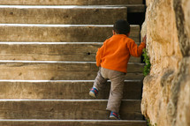 a toddler boy walking up steps outdoors 