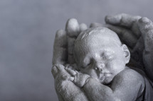 Sculpture of hands holding a newborn baby.