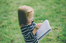 Girl standing outside writing in a spiral notebook.