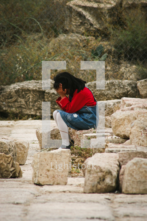 a little girl crying sitting on rocks 