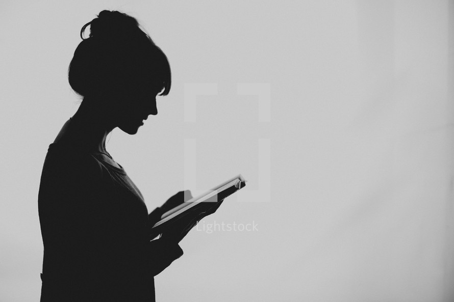 A young woman silhouetted reading her Bible