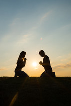 a couple kneeling in prayer together at sunset 