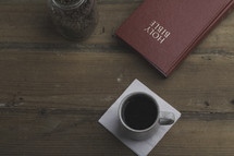 coffee beans in a mason jar, coffee mug on a napkin, and Holy Bible on a table 