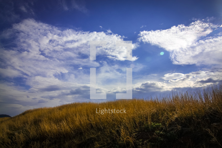 grassy hill against blue sky with clouds