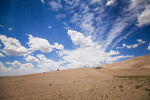 people in the distance walking down a sand dune 
