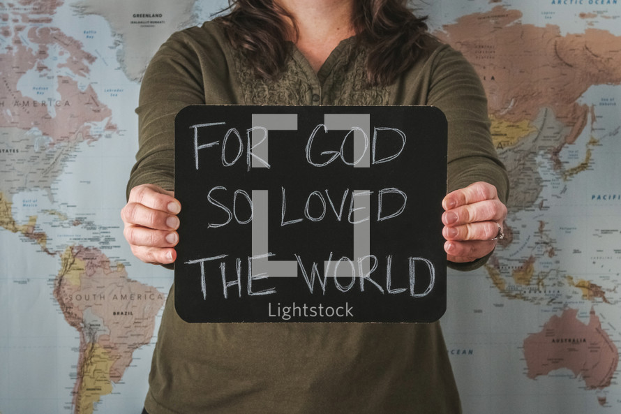 A woman in front of a world map holding a sign - For God so loved the world 