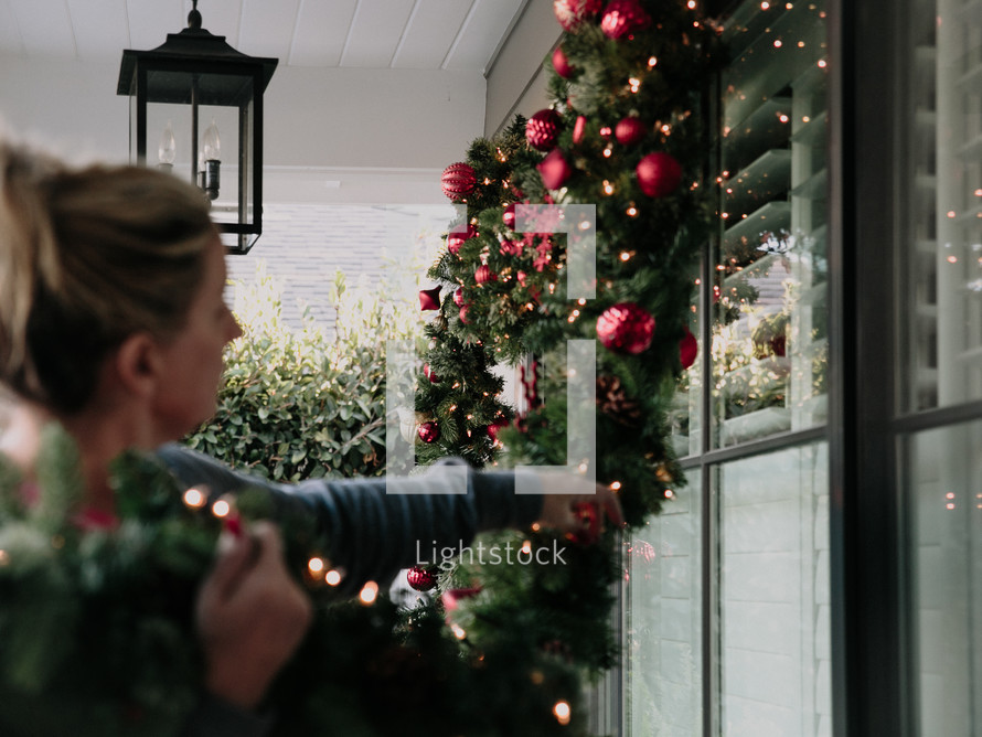 A woman decorates her house with a Christmas garland.