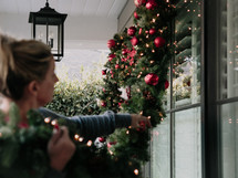 A woman decorates her house with a Christmas garland.